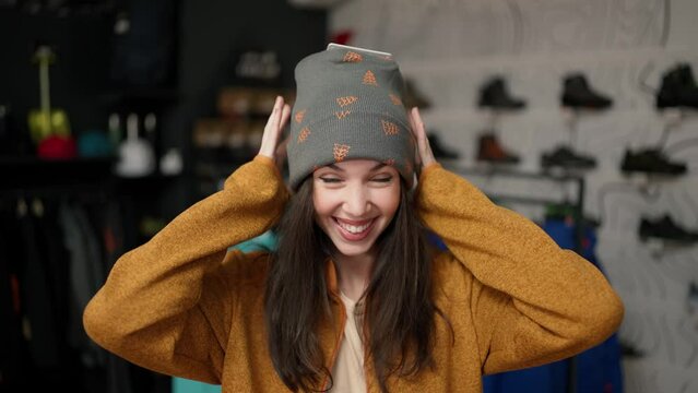 Front view of a smiling woman trying on a new colorful winter hat in a store