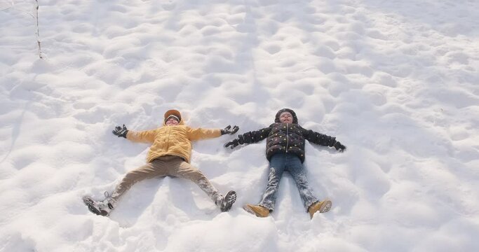 Happy kids doing snow angel. Active outdoors in winter, winter holidays, 4k slowmotion