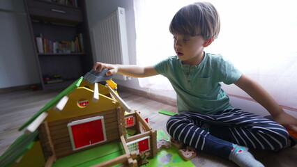 Child playing in room with mother building traditional wooden home toy. Little boy builds house with parent 2