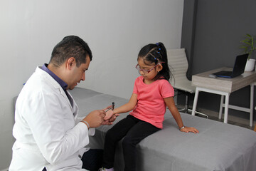 Latino doctor medic and girl patient in medical office checks her reflexes on hammer in her checkup to find disease diagnosis
