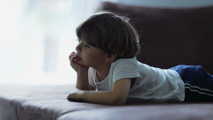 One small boy closeup face with hand in chin watching screen off camera. Focused child hypnotized by TV media content