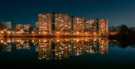 Night view on Tysiaclecie estate in Katowice, Silesia, Poland. Lightened residential buildings with surrounding trees at dusk seen through the lake.