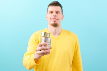 A man holding two steel cans on a blue background. Canned food. Cylindrical. Loaded. Eating....