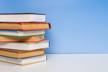 Stack of books in the colored cover lay on the wooden  table and blue backround. Education learning concept