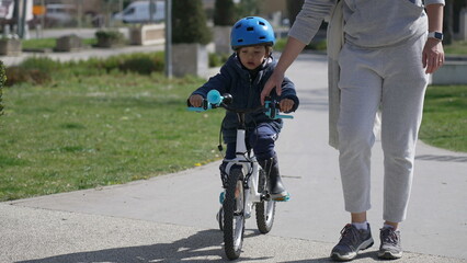 Little boy learning to ride bicycle with mother support. Mom helping child to ride bike outdoors