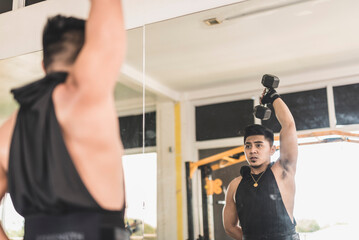 A fit asian man does a single arm overhead dumbbell tricep extension, with one hand behind the waist. Training arms at the gym.