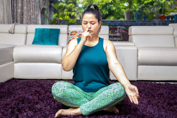 Young indian woman in sportswear sitting in Sukhasana pose, Alternate Nostril Breathin exercise at...