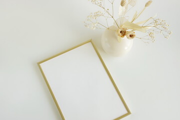 Frame mockup with copy space and vase with dried flowers in beige colors top view on beige background.Minimal interior template