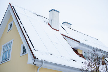 Close-up of snow covered solar panels installed on historic building gable roof with chimney....