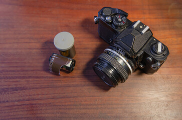 Film camera and 35 mm film roll on wooden table