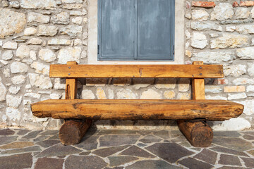 Close-up of an empty wooden bench made of tree trunks in front of a mountain cottage (stone house)....