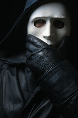 Man in terrible face mask staring at camera against dark background cloak with hood