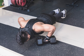 A buff and tanned man does 45 degree pushups on hex dumbbells acting as a push up handle. Chest, anterior deltoid and tricep training.