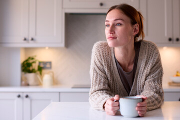 Young Woman Relaxing At Home In Kitchen Holding Hot Drink