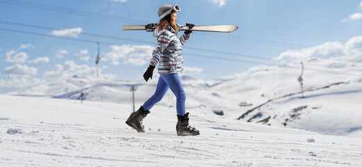 Young female with carrying skis and walking on a snowy hill