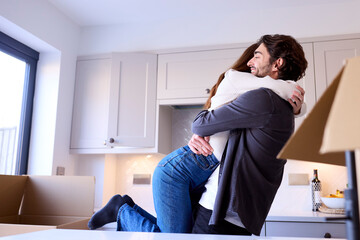 Young Couple Moving Into New Home Hugging As They Unpack Boxes In Kitchen Together