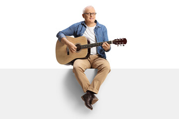Mature man playing an acoustic guitar and sitting on a blank panel