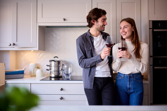 Romantic Young Couple At Home Celebrating With Glass Of Wine In Kitchen Together