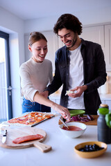 Couple In Kitchen At Home Making Homemade Pizza Together