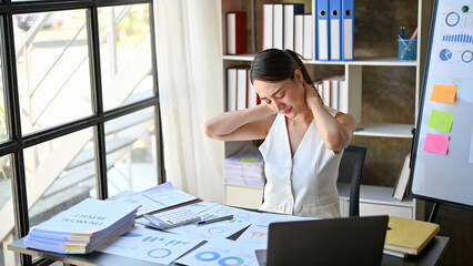 Overworked and tired Asian businesswoman massaging her neck, suffering from neck ache.