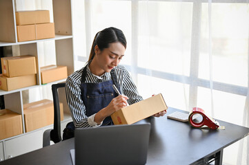 Asian female online business owner writing customer's address on a cardboard box