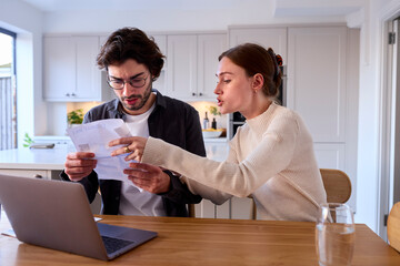 Worried Couple At Home Looking At Laptop Holding Energy Bill