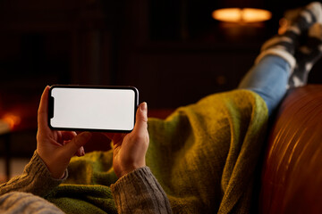 Close Up Of Woman At Home Lying In Lounge With Cosy Fire Streaming Onto Blank Screen Mobile Phone