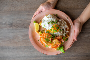 Top view of unrecognizable woman holding plate with yummy sunny side up eggs, piece of lime, salmon, tomato. Cooking.