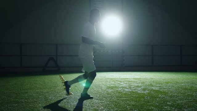 athletic black man running in indoor football training area, practicing ball pass, slow motion