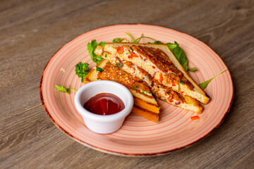 Close-up of pink plate with appetizing fried sandwiches, ketchup in little white bowl decorated with greenery on table.
