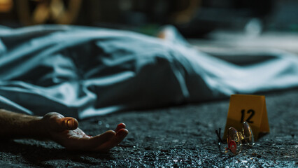 Cold Toned Picture: A Corpse Lying on the Floor and Covered. Victim's Hand is Peeking Out. Accidental Manslaughter Leaving Young Man for Dead. Glasses and Blood Marked as Evidence Next to the Corpse