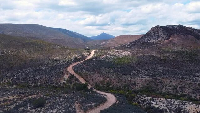 Tracking shot flying forward over a car driving on a curvy dirt road , near a warehouse, in Cloetesberg, on edge of the klein karoo semi desert region and garden routes, Western Cape, South Africa.