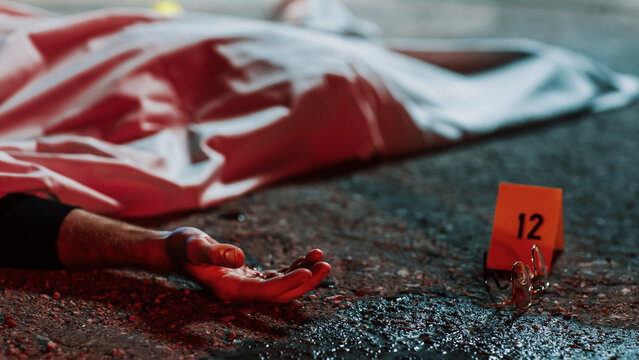 Close Up Low Angle: A Corpse with a Bloody Hand Lying on the Floor and Covered. Gruesome Murder Case Leaving Victim for Dead. Glasses and Blood Marked as Evidence Next to the Corpse. Cinematic Shot