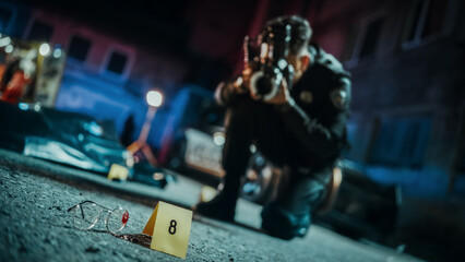 Policeman Taking Photos of Marked Evidence on a Crime Scene at Night. Forensics Police Officer Finds Glasses Potentially Belonging to the Dead Victim and Photographs it for Analysis. Focus on Glasses