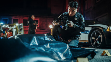 Obraz na płótnie Canvas Wide Angle Portrait Shot of an Asian Young Police Officer Doing Forensic Work and Taking Photos of Marked Evidence. Crime Scene Investigation Unit Collaborating in the Background with Paramedics
