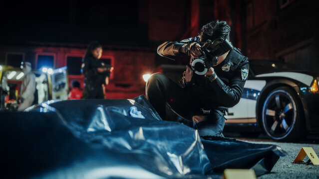 Policeman Taking Photos of Bagged Corpse Found Murdered in a Back Alley at Night. Police Officer at Crime Scene Documenting the Victim's Body. Death of a Bystander Caused by Gang War and Firearms