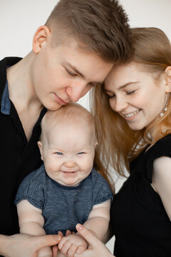 Portrait of happy family from three in black looks on white background. Mom and dad gently touch little hands of joyful smiling infant baby closeup. Parental affection, childcare, firstborn