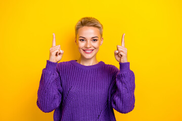 Photo of attractive smiling promoter lady wear purple knit sweater fingers indicate good news up empty space ad isolated on yellow color background