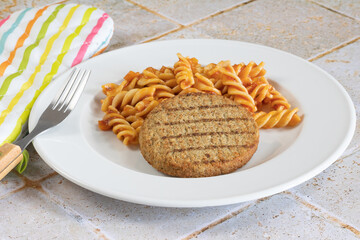 steak haché végétal et pâtes à la tomate dans une assiette
