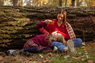Naklejka na ściany i meble Smiling cheerful, relaxed woman and girl, mother and daughter lying and stroking together near tree trunk during weekend