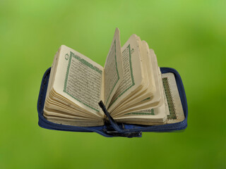 Mini opened Al-Qur'an on green background. Blue colors of Al-Qur'an.