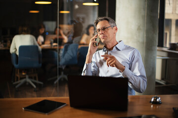 Fototapeta na wymiar Businessman in office. Handsome man talking on phone at work..