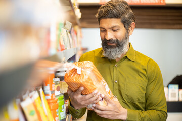 Mature Indian man buying at grocery shop. Asian male check price of bread food purchase at...