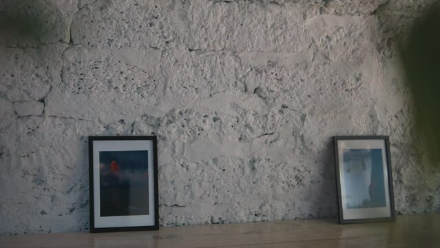 Two pictures framed, on a wooden floow, leaning on a retro white brick wall, in a empty room