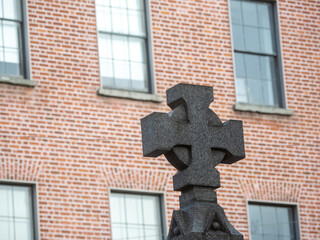 Dark concrete cross i focus. Red brick building out of focus in the background.