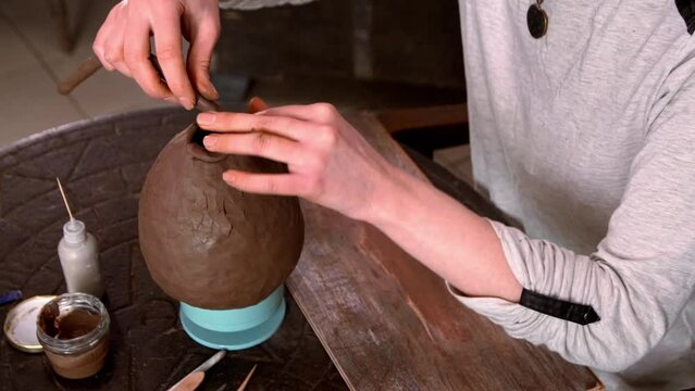 Female hands handle the edge of a wet clay bowl with a stick. Female hands hold a bowl for casting clay products. Shaped method for making clay dishes