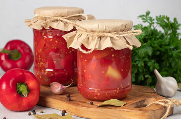Pickled sweet peppers with tomatoes in two glass jars on gray background