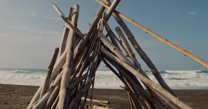 A close up shot of a stack of sticks creating a triangle. Waves in the background decorate the scenery.