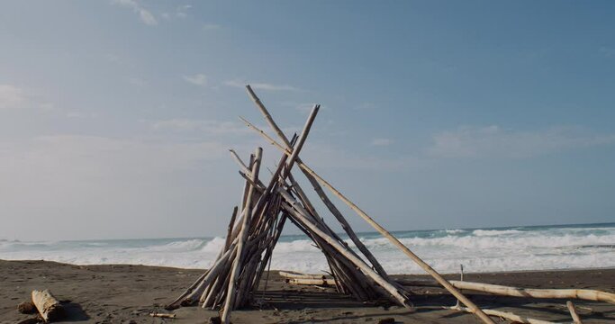 A wide shot of a stack of sticks creating a triangle. Waves in the background decorate the scenery.