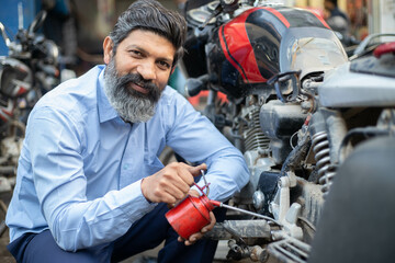 Fototapeta na wymiar Professional Indian mechanic repairs motorcycle give oil to it. Asian man repairing motorbike in repair shop.